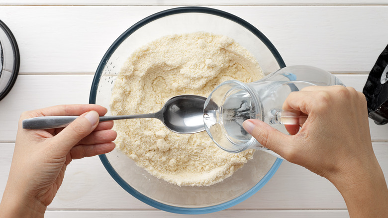 Person adding water to flour