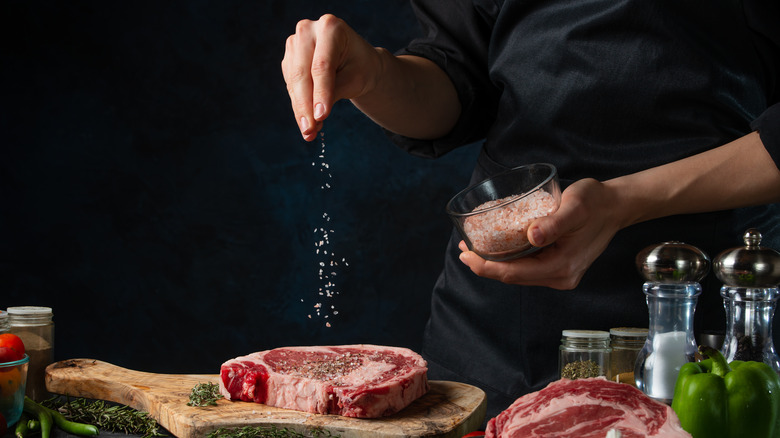 chef hand sprinkling salt on raw steak