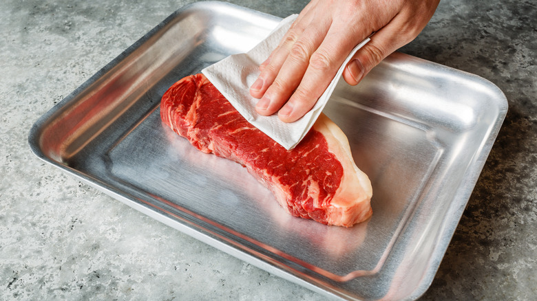 hand patting meat dry with paper towel