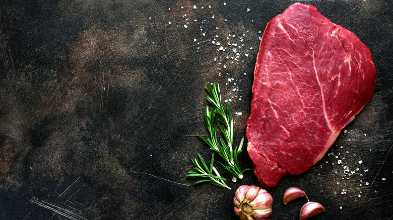 raw steak next to spices, herbs and garlic