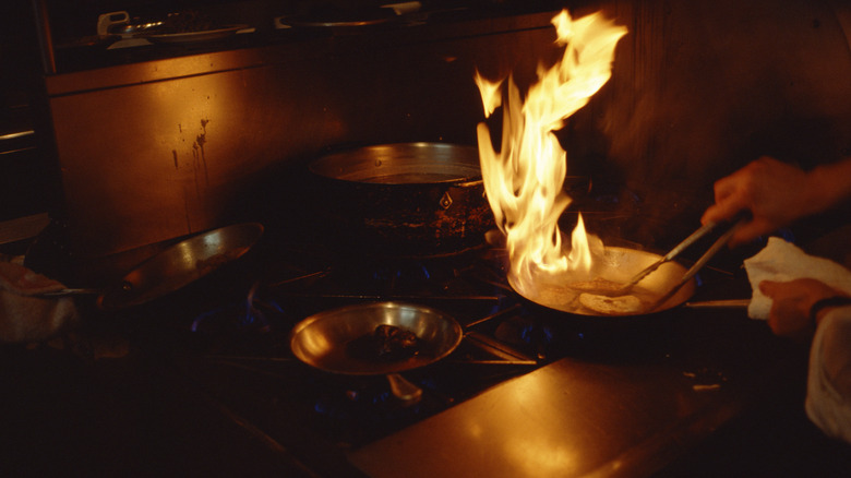 Chef cooking with a blaze of fire in a frying pan 
