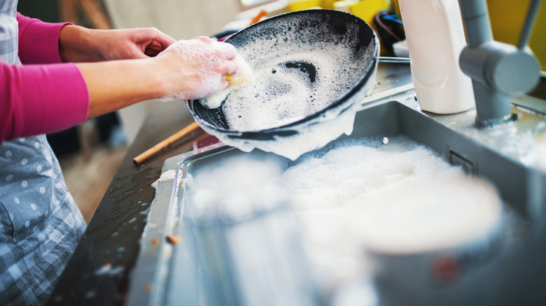 woman with yellow kitchen gloves washing a pan in soapy water