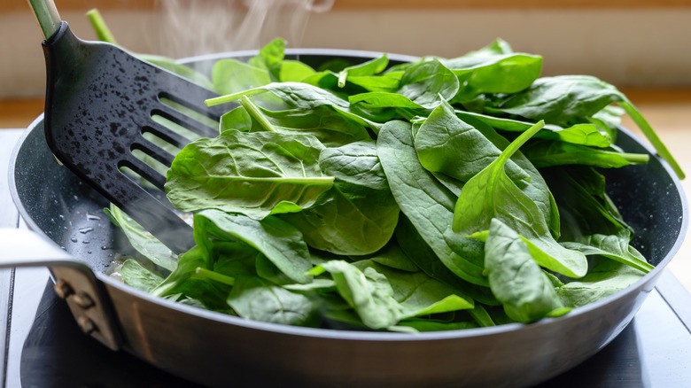 spinach in hot pan being flipped with spatula