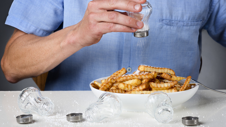 Person shaking salt over fries