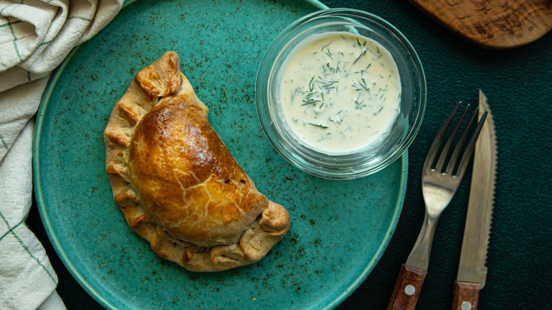 An empanada on a plate with dipping sauce on the side