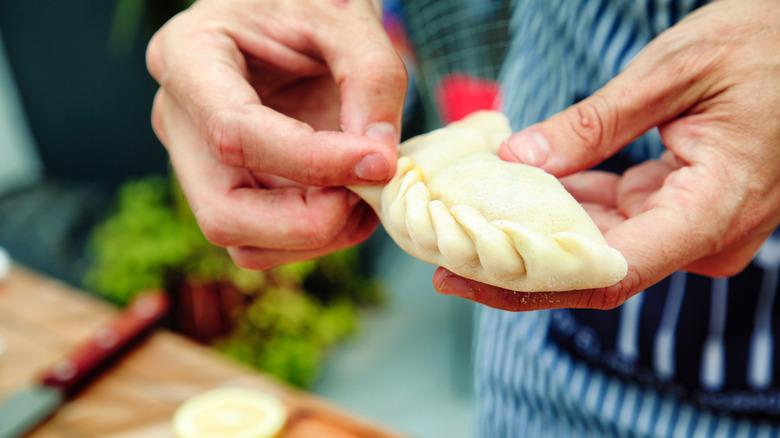 Hands sealing an empanada