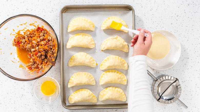 Egg washing empanadas on a baking sheet