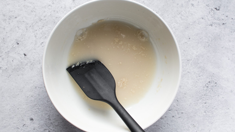 Yeast and water in a white bowl with a black spatula