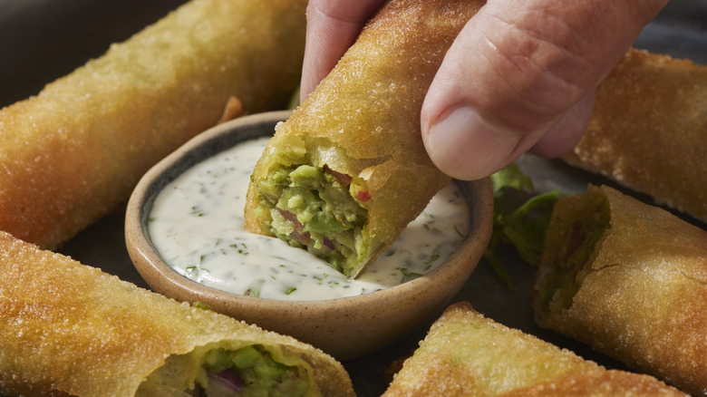 Hand dipping an avocado spring roll into ranch dressing