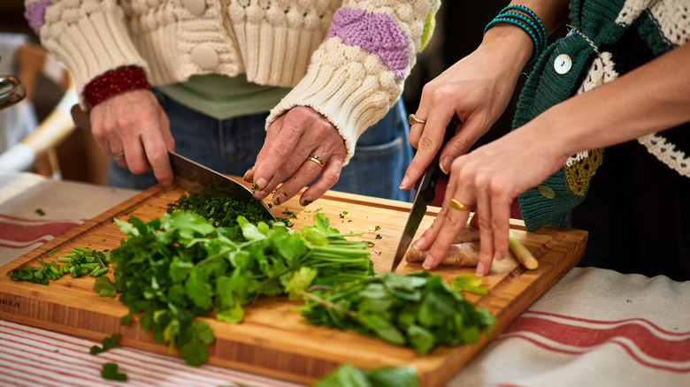 Two pairs of hands chopping fresh herbs