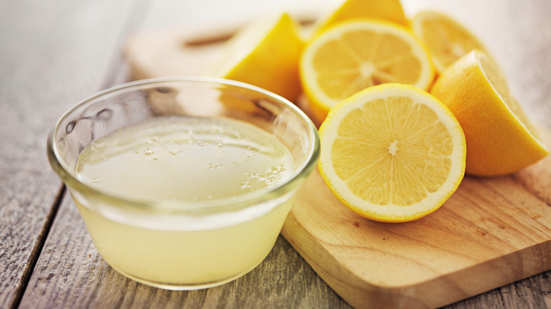 Bowl of lemon juice next to halved lemons