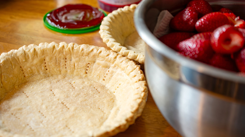 A baked pie crust next to a pot of strawberries