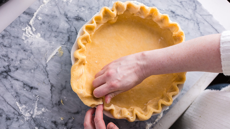 Hands shaping a pie crust into a pan