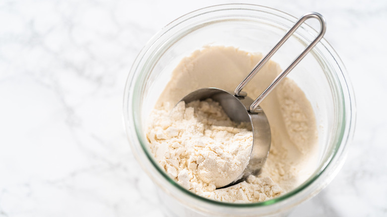 A metal measuring cup in a glass jar of flour