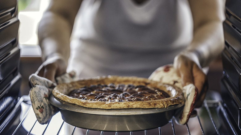 Hands reaching into an oven for a pecan pie