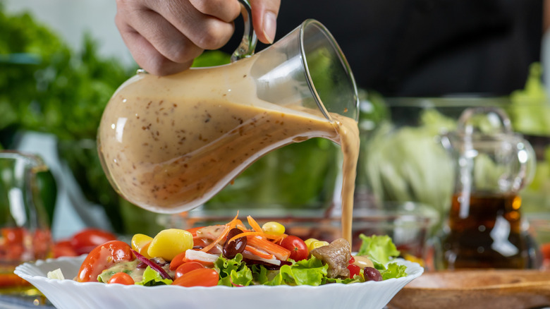 Salad dressing being poured onto greens