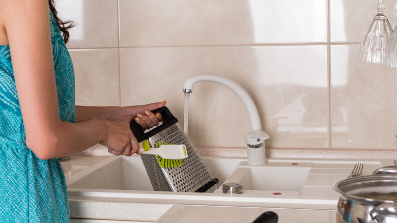 person washing grater in sink