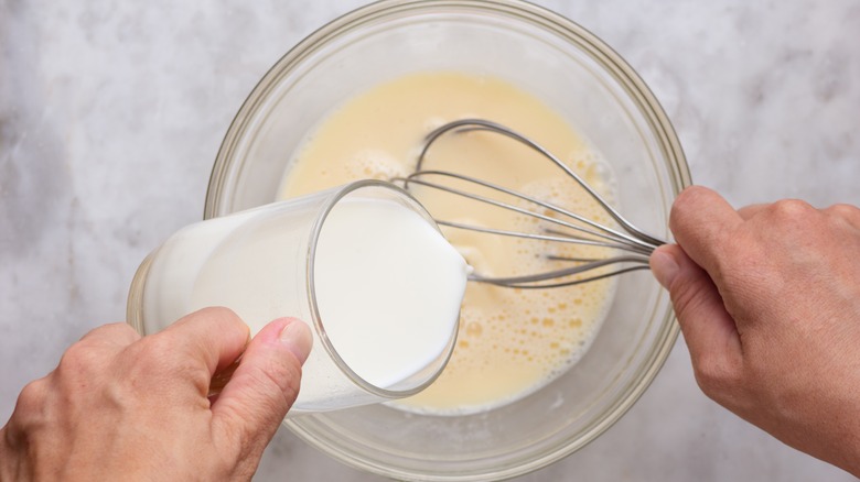 Pouring milk into a batter in a bowl with a whisk