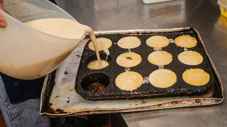 Batter being poured into muffin tray with hot oil from a jug