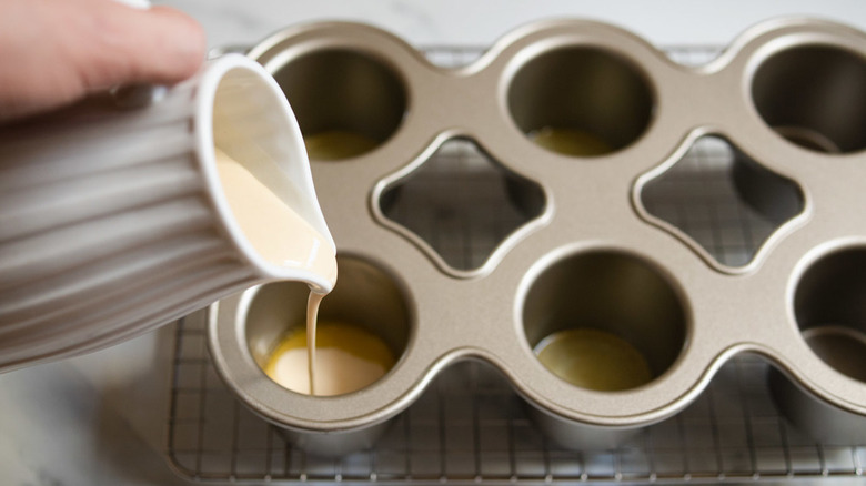 Batter being poured from a jug into a muffin tin tray