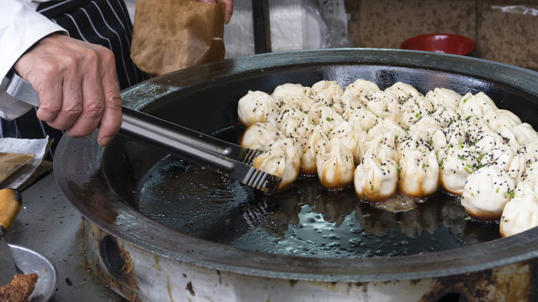 chef using tongs to turn dumplings in pan