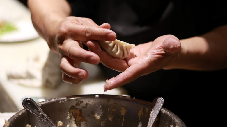 hands holding dumpling over pot of meat filling