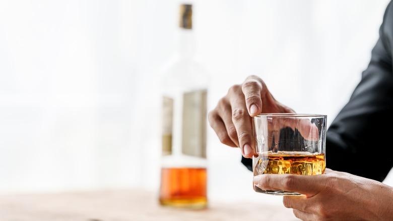 person drinking whiskey with bottle in background