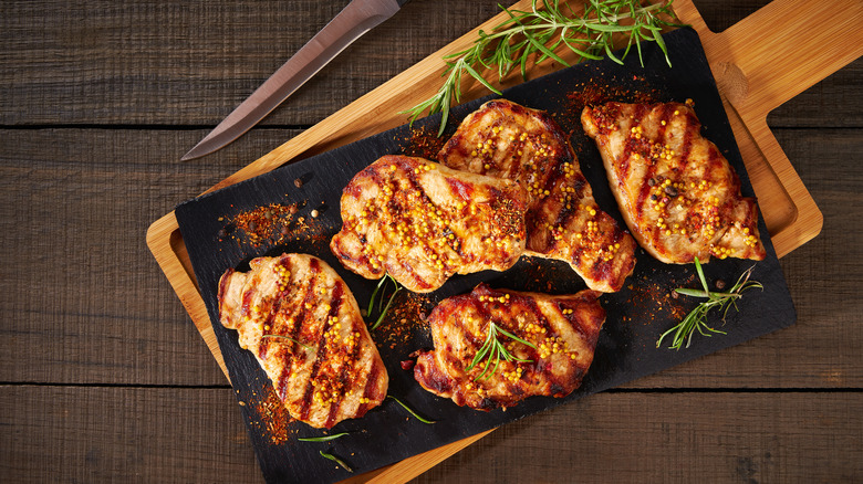 grilled pork chops on slate and wooden cutting board with rosemary sprigs and knife