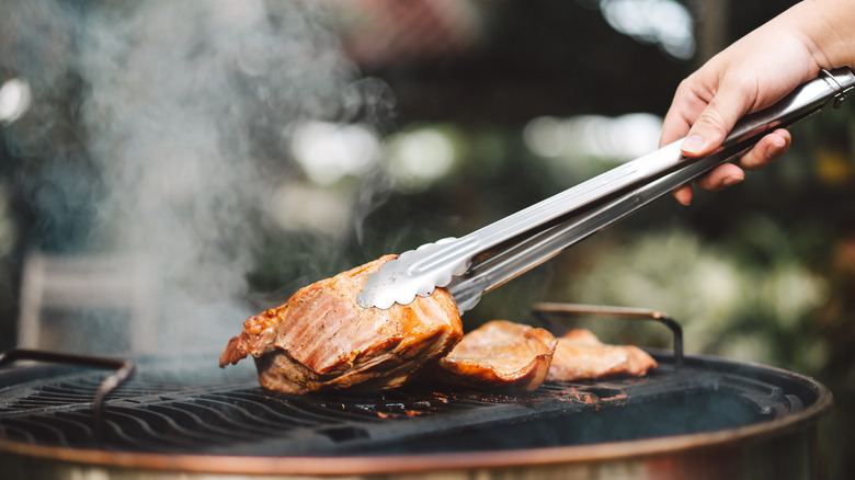 hand turning meat on grill with tongs