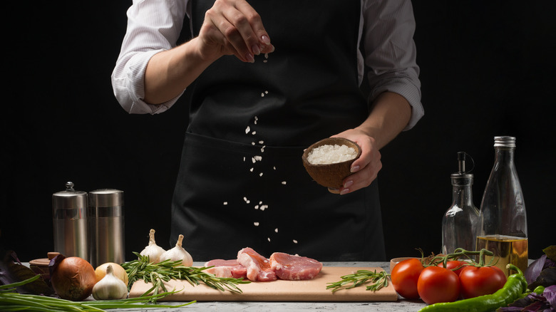 person salting pork sitting on wood cutting board