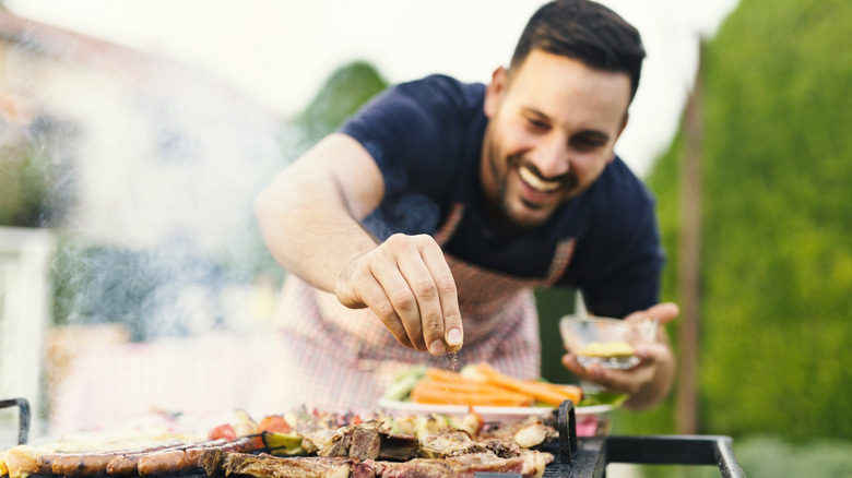 man adding seasoning to meat on grill