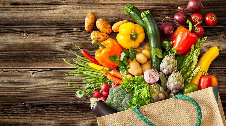 Vegetables spilling out of canvas bag onto unfinished wood surface