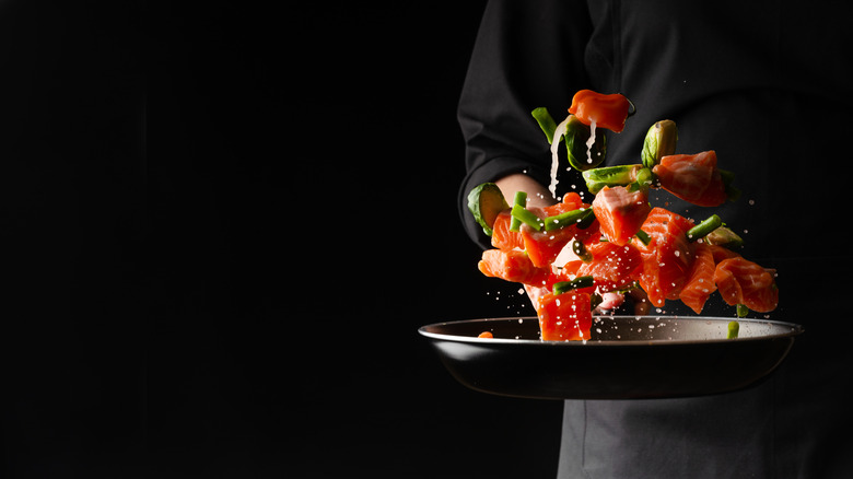 chef tossing fish and vegetables in pan on black background