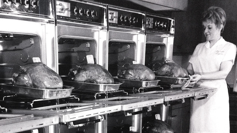 Black and white photo of woman next to turkeys in ovens