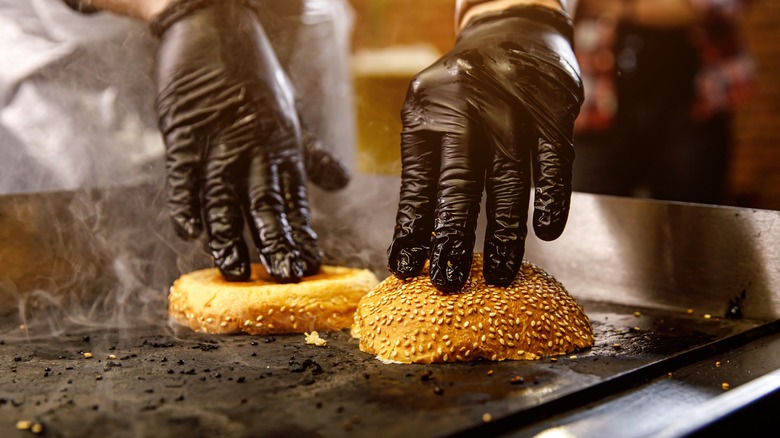 chef pressing down burger buns on a flat griddle to toast