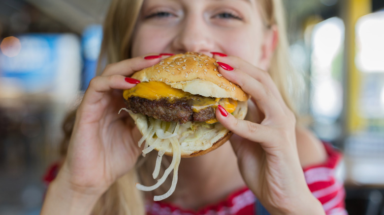 person eating burger with onions falling out 