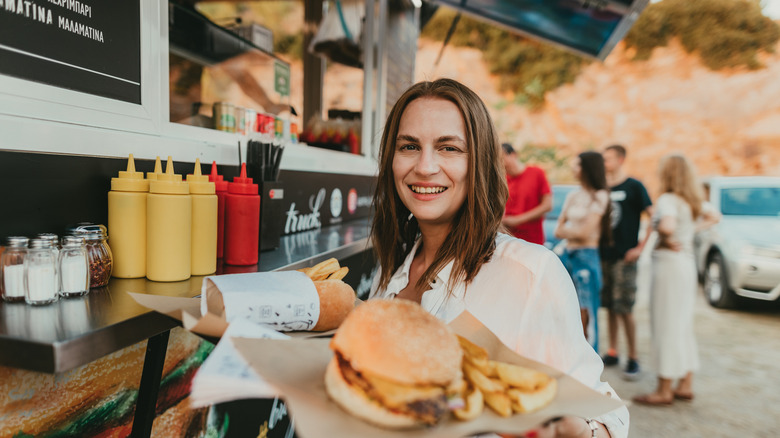 person holding burger and fries on paper outside a food truck