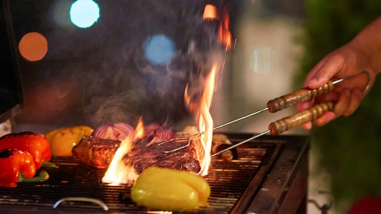 Flipping meat with tongs over fiery grill