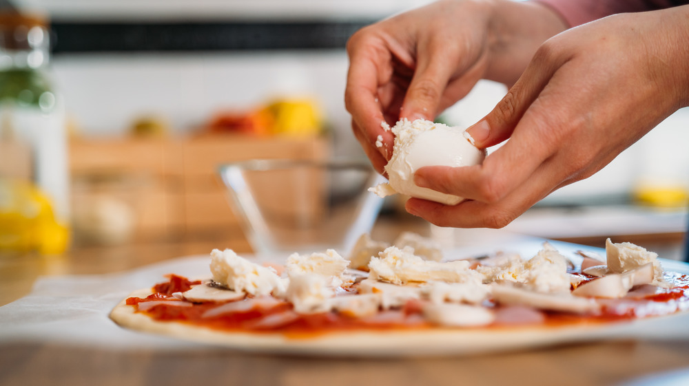 Woman adding cheese to a pizza