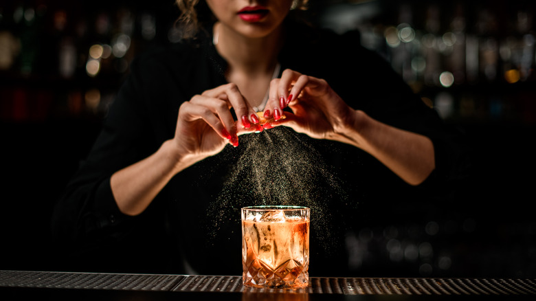 Female bartender squeezes an orange peel into 