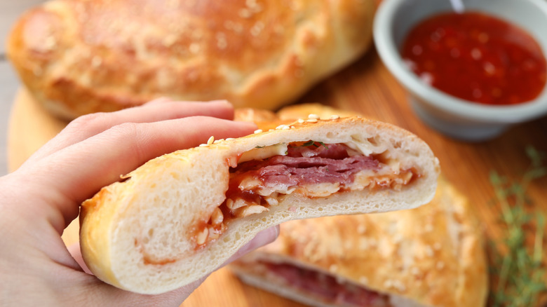 Hand holding a calzone with dipping sauce in the background