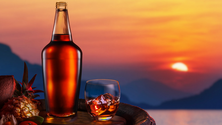 rum bottle with glass of ice in front of a sunset over mountains