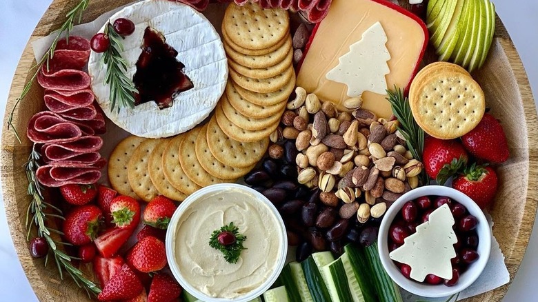 close up of Christmas charcuterie board with bowl of creamy dip, Christmas brie, ruffled salami, gouda, crackers, sliced apples, and other ingredients