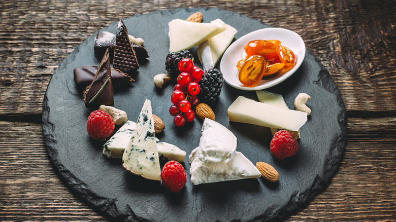 round slate plate with assorted cheeses, fresh fruit, candied kumquats, almonds, and wedges of chocolate