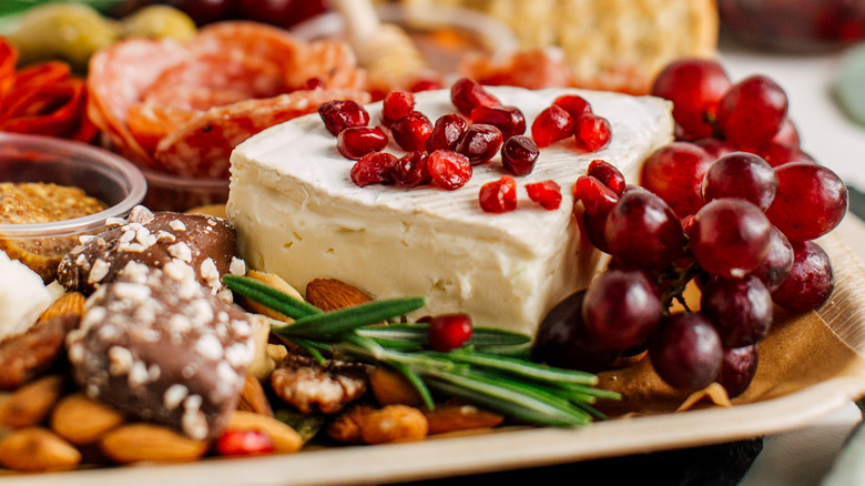 close up of charcuterie plate with focus on wedge of brie garnished with pomegranate seeds and fresh rosemary sprig