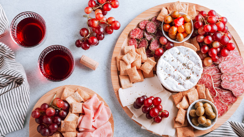 wooden charcuterie board with cured meats, crackers, cheese, olives, and red grapes on white table with two glasses of red wine