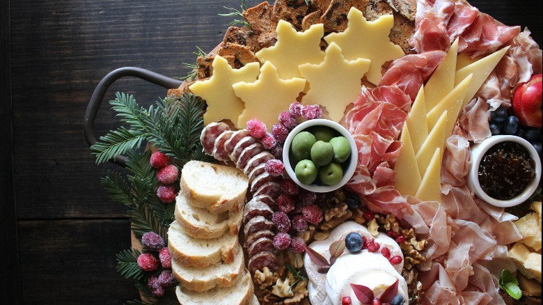 Christmas themed charcuterie board with sugared cranberries, bread, snowflake shaped cheese, crackers, meat, and other ingredients