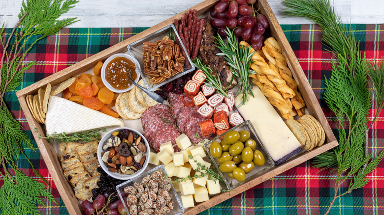 charcuterie board with cheeses, meats, crackers, dried fruit, toasted pecans, candied almonds, and other ingredients on green and red tartan table runner with fresh greens