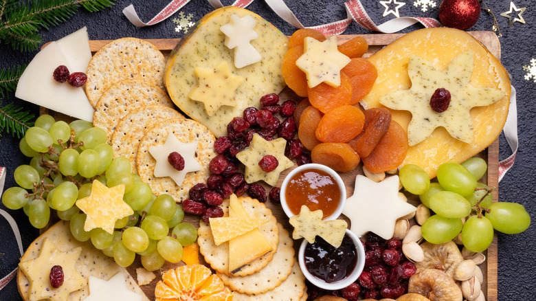Christmas charcuterie board with crackers, star shaped cheese cut outs, fresh grapes, small bowls of jams, dried cranberries, and dried apricots