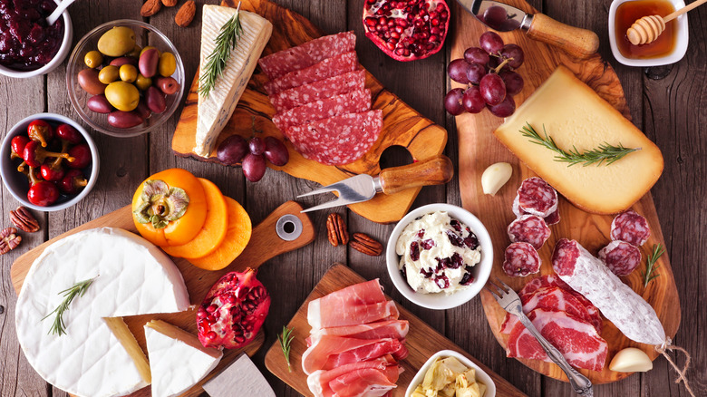 grazing table with bowls of chutney, olives, pickles, honey, and soft whipped cheese, plus cured meats, persimmon, grapes, and other types of cheeses
